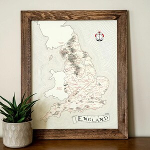 May include: A framed map of England with a compass rose in the top right corner. The map is in black and white with red markings. The frame is made of dark wood.