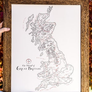 May include: A framed map of the Island of Great Britain with a detailed black and white illustration of the country's regions and borders. The map is printed on white paper and has a red title and compass.