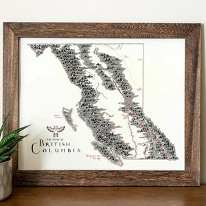 May include: A framed black and white map of British Columbia with a red and black stylized bird illustration in the bottom left corner. The map shows the province's mountains and rivers. The text "The Land of British Columbia" is printed below the bird illustration.