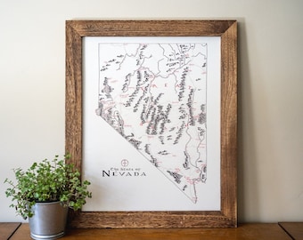 May include: A framed map of the state of Nevada with a black and white outline of the state and red text. The text at the bottom of the map reads "The State of Nevada".