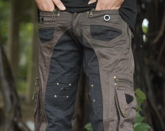 May include: Brown and black cargo pants featuring multiple zippered pockets, metallic grommets, and brass-toned studs. The design includes ribbed fabric panels at the knees, reinforced stitching, and a structured waistband with zipper closures.