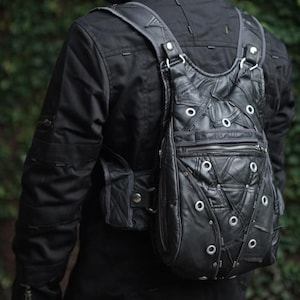 Op de afbeelding: Zwarte leren rugzak met een uniek patchwork ontwerp. De tas heeft zilverkleurige ogen en een voorvak met ritssluiting. De riemen zijn verstelbaar en de tas wordt over de schouder gedragen. De algehele stijl is edgy en modern.