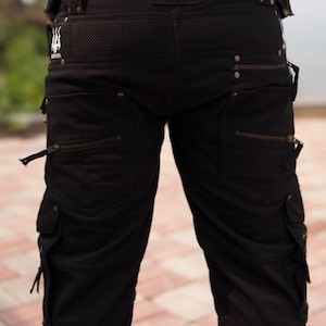 May include: Black cargo shorts with multiple pockets and zippers. The shorts feature a mesh panel at the back and a logo patch that reads "MAARI MAV". The shorts have a casual, yet rugged design.