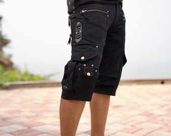 May include: Black cargo shorts featuring multiple utility pockets, silver-toned metal zippers, and snap button closures. The shorts include decorative mesh panels, reinforced stitching, and metal rivets along the pockets and waistband area.