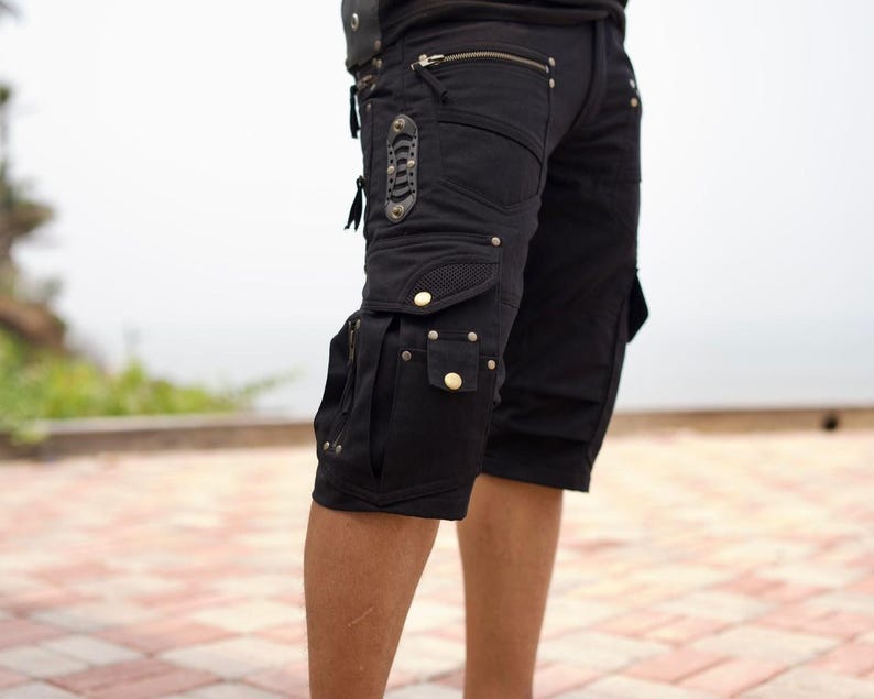 May include: Black cargo shorts with multiple pockets, zippers, and decorative rivets. The shorts have a knee-length cut and a utilitarian design, suitable for outdoor activities or casual wear.