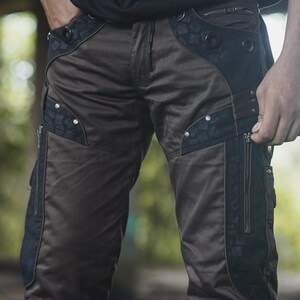 Peut inclure: Pantalon cargo marron avec des détails noirs et des rivets argentés. Le pantalon comporte plusieurs poches zippées et des panneaux décoratifs. Le design comprend un motif unique sur les panneaux noirs, ajoutant une touche élégante.