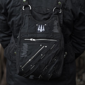 Peut inclure: Sac à bandoulière noir avec plusieurs fermetures éclair argentées, des rivets et un emblème de trident. Le sac a des bretelles réglables et une poche avant. Fabriqué dans un matériau durable, possiblement résistant à l'eau.