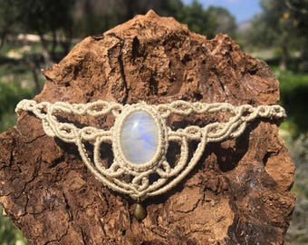 Puede incluir: Un collar gargantilla de macramé blanco con un colgante de piedra lunar ovalado grande. El collar está hecho con un cordón de fibra natural y tiene un diseño delicado e intrincado.