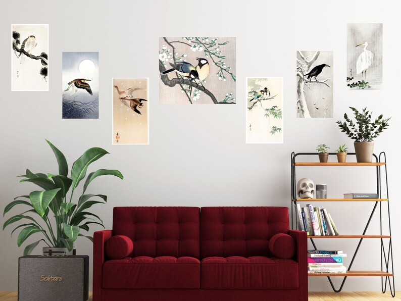May include: A set of eight framed prints featuring Japanese-style illustrations of birds and flowers. The prints are arranged on a white wall above a red couch and a wooden shelf with books and decorative items.