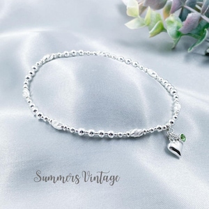 May include: A silver beaded anklet with a heart charm and a small green gemstone. Summers Vintage.