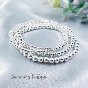 May include: A set of four silver bead bracelets stacked on top of each other. The bracelets are made of small, round beads and are all the same size. The bracelets are on a light grey background.
