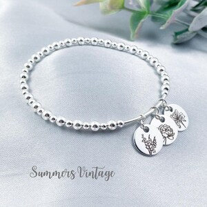 May include: A silver beaded bracelet with three silver charms featuring engraved floral designs. The charms include a butterfly, a peony, and a sprig of flowers.
