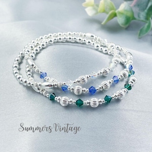 May include: Three silver beaded bracelets with crystal accents. The bracelets feature alternating silver beads and blue and green crystals.