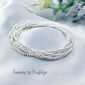 May include: A silver beaded bracelet with multiple strands of small, round beads. The bracelet is wrapped around itself, creating a layered effect.
