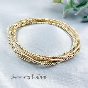 May include: Gold beaded bracelet set. The bracelets are made of small, round, gold-coloured beads. The set includes multiple strands of beads, creating a layered look. The bracelets are displayed on a light-coloured, textured surface. The text "Summers Vintage" is visible.