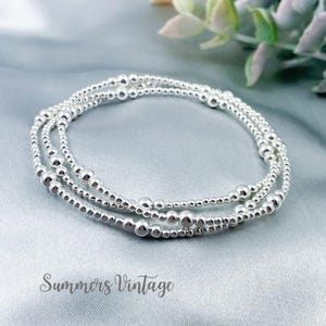 May include: Three silver beaded bracelets. Each bracelet is made of small, round, shiny silver beads. The bracelets are stacked. The background is a light blue fabric. The text "Summers Vintage" is at the bottom.