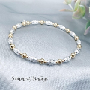 May include: A delicate bracelet with alternating gold and silver beads. The bracelet has small, round gold beads and larger, faceted silver beads. The text "Summers Vintage" is at the bottom of the image.