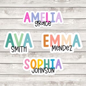 May include: Four custom name stickers featuring colorful block letters for the first names Amelia, Ava, Emma, and Sophia, with the last names Grace, Smith, Mendez, and Johnson printed in a smaller black script font underneath each name.