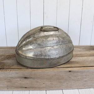 May include: A vintage silver metal bread loaf pan with a fluted design and a handle on the top. The pan is sitting on a wooden surface.
