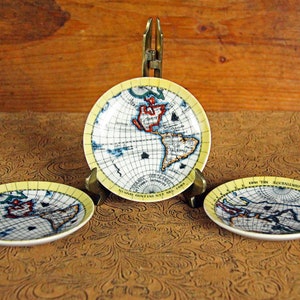May include: Three small, round decorative plates with a world map design. The plates have a yellow border and feature continents in red, blue, and green. The plates are displayed on a brown surface.