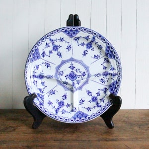 May include: A white and blue divided serving platter with a floral design. The platter is supported by a black wooden stand. The blue floral pattern includes flowers and leaves, with a scalloped edge.
