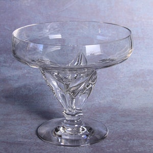 May include: A clear glass pedestal bowl with a swirling, textured base. The bowl is round and has a wide rim.