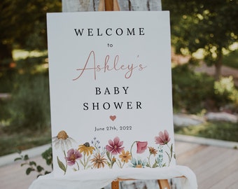 May include: A white sign with a floral border and the text "Welcome to Ashley's Baby Shower June 27th, 2022".