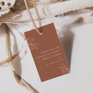May include: A terracotta-colored gift tag with a leather string, featuring the text "THANK YOU FOR COMING TO CLAIRE'S BRIDAL SHOWER" and the date November 27, 2020. The tag has a minimalist floral design.