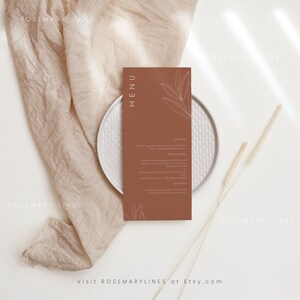 May include: A brown menu card with a white outline of a leaf design. The text "MENU" is in white and the text "STARTERS", "MAIN COURSE", and "DESSERTS" are in white. The text "Visit ROSEMARYLINES at Etsy.com" is at the bottom of the card.