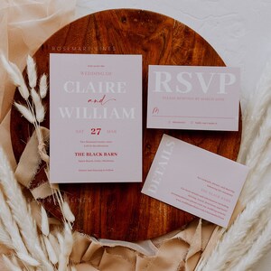 May include: A wedding stationery set in shades of pink, including an invitation, RSVP card, and details card. The cards are displayed on a wooden charger. The invitation announces the wedding of Claire and William on 27th March.