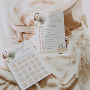 Puede incluir: Dos tarjetas de juego de despedida de soltera imprimibles con tem&aacute;tica oto&ntilde;al. La primera tarjeta es una tarjeta de bingo con un dise&ntilde;o de calabaza y flores. La segunda tarjeta es un juego de m&aacute;s o menos con un dise&ntilde;o de calabaza y flores. El texto de la segunda tarjeta dice "M&aacute;s o Menos".