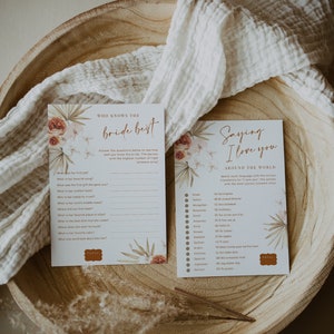 May include: Two cards with floral accents and text, one titled "Who Knows the Bride Best" and the other "Saying I Love You Around the World." The cards are on a wooden tray with a white cloth.