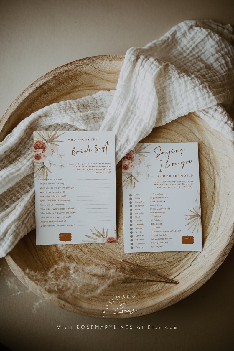 May include: Two cards with floral accents and text, one titled "Who Knows the Bride Best" and the other "Saying I Love You Around the World." The cards are on a wooden tray with a white cloth.