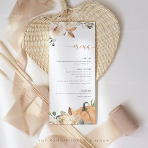K&ouml;nnte beinhalten: Eine Men&uuml;karte mit einem Aquarell-K&uuml;rbis- und Blumendesign. Das Men&uuml; bietet Vorspeisen, Hauptgerichte und Desserts. Die Karte ist mit beigen und orangefarbenen Blumen und Bl&auml;ttern verziert. Der Text "menu" ist in Schreibschrift geschrieben.