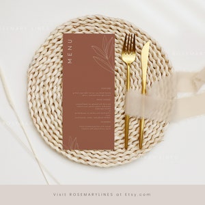 May include: A brown menu card with a simple line drawing of leaves on a white background. The card is on a woven placemat with a gold fork and knife.