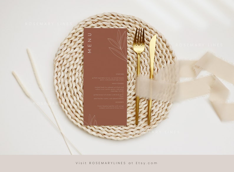 May include: A brown menu card with a simple line drawing of leaves on a white background. The card is on a woven placemat with a gold fork and knife.