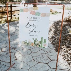 Pu&ograve; includere: Un cartello di benvenuto per un baby shower con un design di cactus e fiori. Il cartello dice "Benvenuti alla festa di Charlotte August 27th, 20XX".