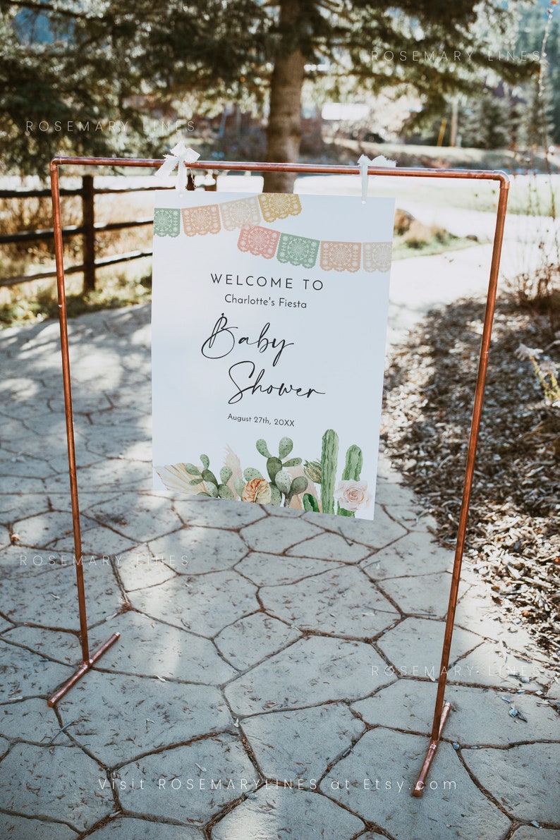 Pu&ograve; includere: Un cartello di benvenuto per un baby shower con un design di cactus e fiori. Il cartello dice "Benvenuti alla festa di Charlotte August 27th, 20XX".