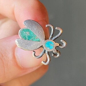May include: A silver butterfly pin with turquoise accents. The butterfly has intricate details and is a beautiful piece of jewelry.