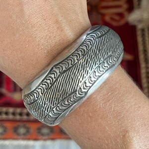 May include: A silver bracelet with an intricate, geometric design. The bracelet is wide and has a rounded shape.