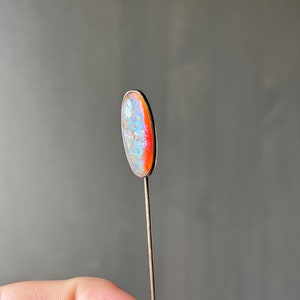 May include: A silver pin with a light blue and orange oval-shaped opal stone.
