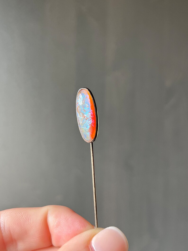 May include: A silver pin with a light blue and orange oval-shaped opal stone.