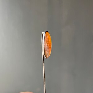May include: A silver tie tack with an oval-shaped orange stone.