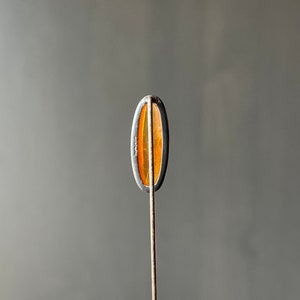 May include: A silver tie tack with an oval-shaped amber stone. The back of the tie tack is marked "Sterling".