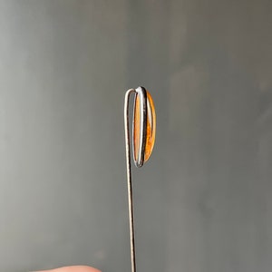 May include: A silver pin with a clear orange oval-shaped stone.