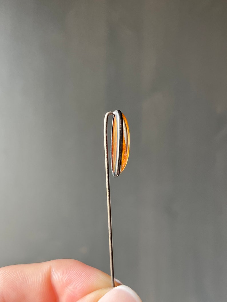 May include: A silver pin with a clear orange oval-shaped stone.