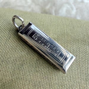 May include: A rectangular silver pendant with a musical staff design. The pendant has a small loop at the top for a chain. The design features a treble clef and musical notes.