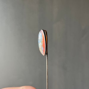 May include: A silver pin with a light pink and blue oval-shaped opal stone.
