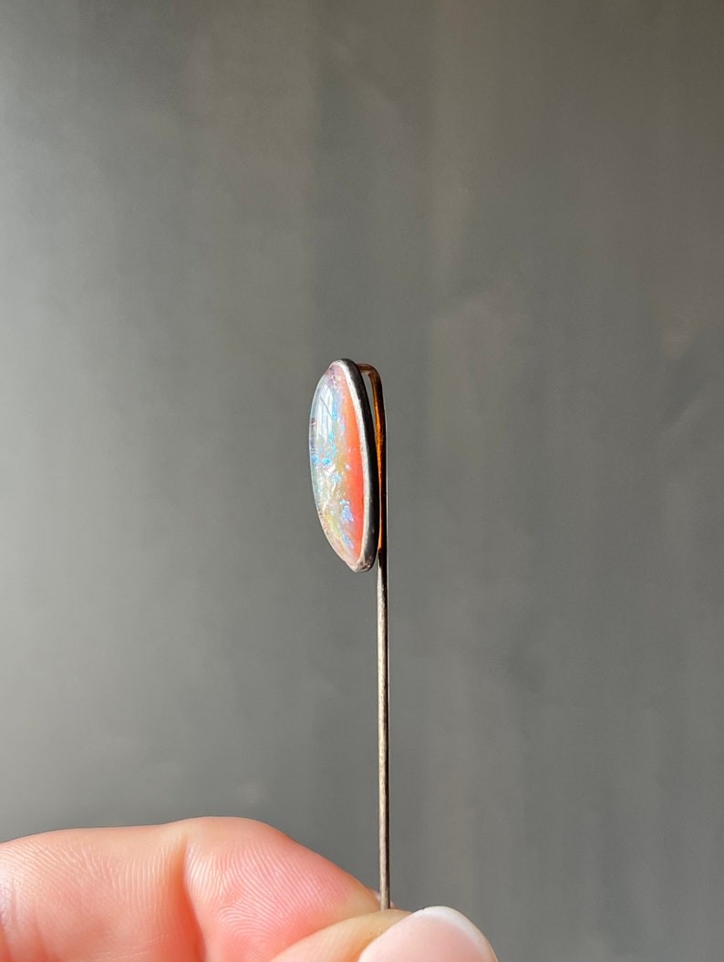 May include: A silver pin with a light pink and blue oval-shaped opal stone.