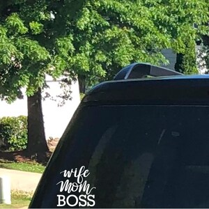 May include: A black vehicle with a white decal that reads "wife mom BOSS" in a cursive font. The image is taken outdoors with a green tree in the background.
